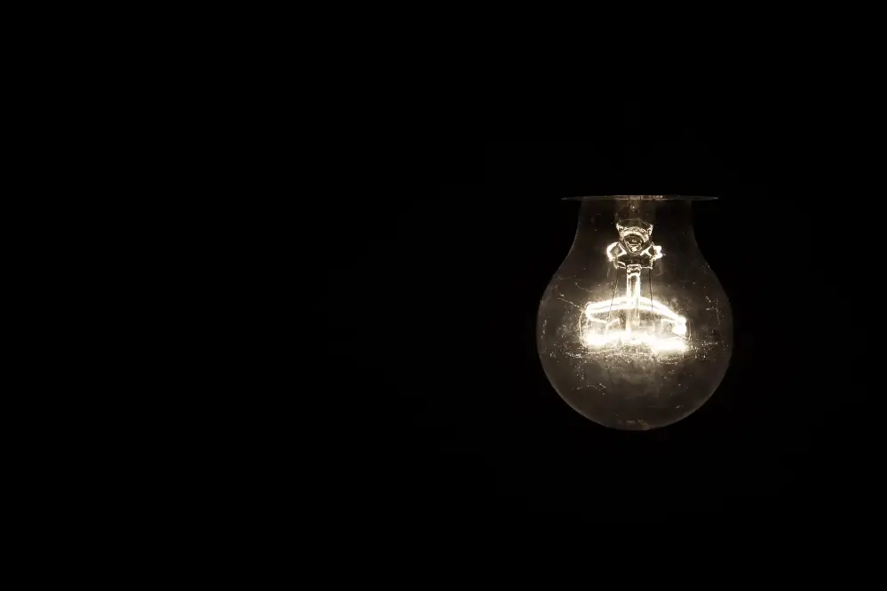 Single light bulb glowing in a dark room symbolising electrical disturbances and flickering lights often linked to signs of a haunting.