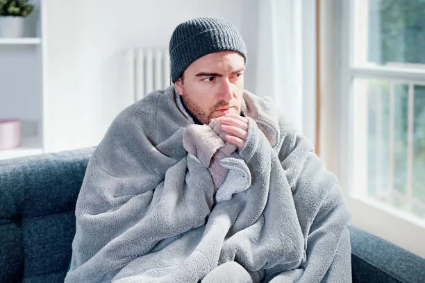 Man wrapped in blanket looking chilled, representing unexplained cold spots in a haunted house.